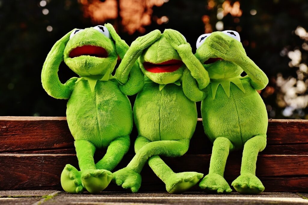 drei grüne Frösche aus Plüsch, die sich Ohren, Augen und Mund zuhalten